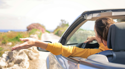 Mujer sacando la mano por la ventana de su descapotable