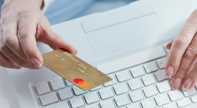 Manos en el teclado del ordenador cogiendo una tarjeta de crédito