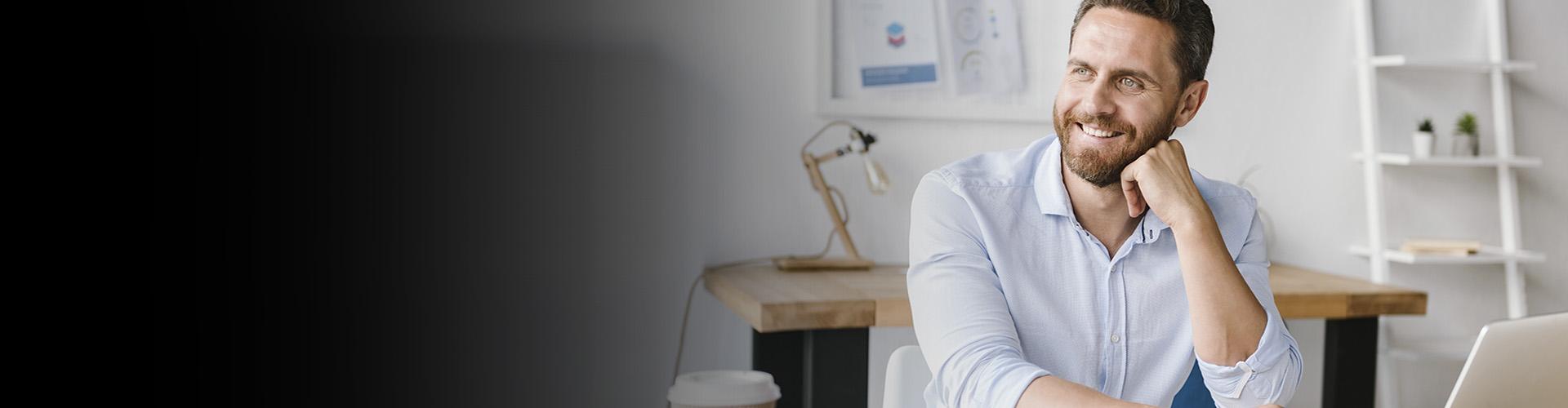 Cuentas Autónomos - Hombre de negocios con barba y camisa blanca sonriendo mientras trabaja frente su portátil