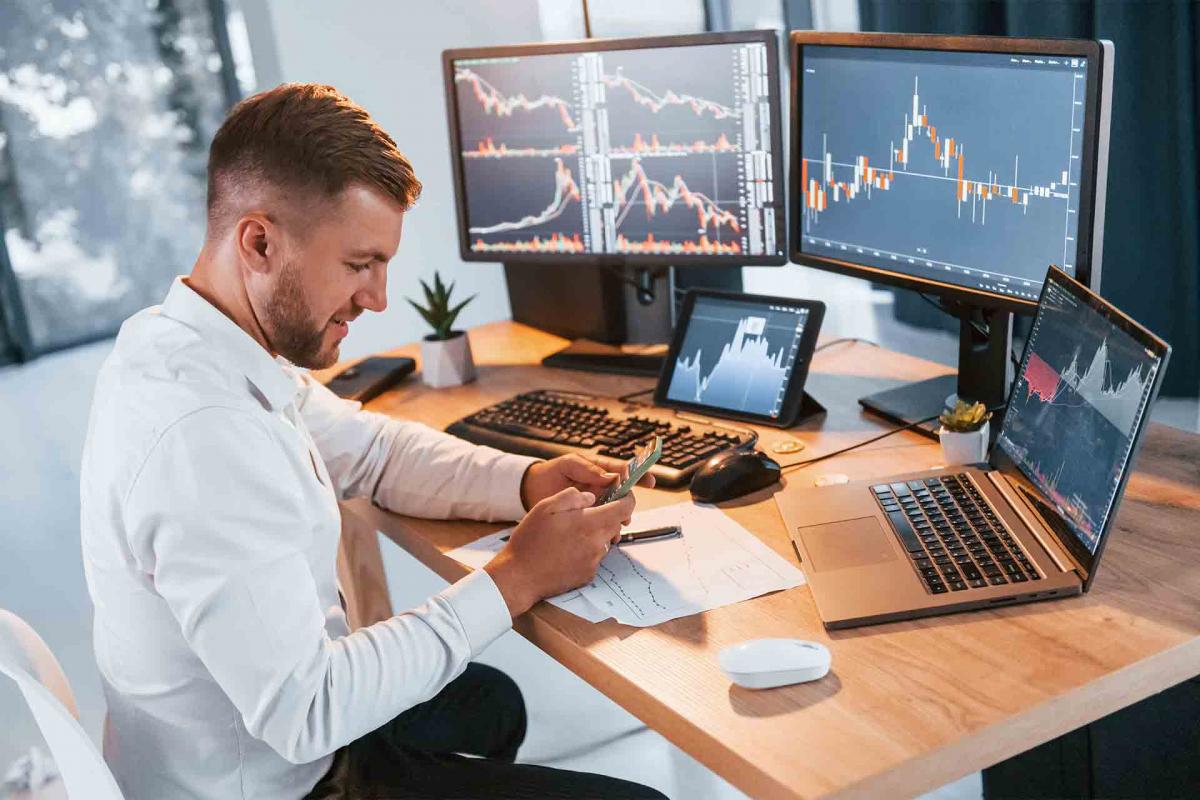 Hombre contento sujetando el móvil con dos monitores de fondo Hombre contento sujetando el móvil con dos monitores de fondo